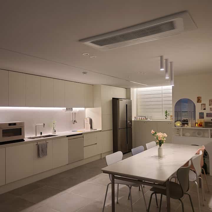 白を基調としたモダンなキッチン、清潔感あるダイニングテーブルと色とりどりの椅子が配置されたカフェ風のインテリア