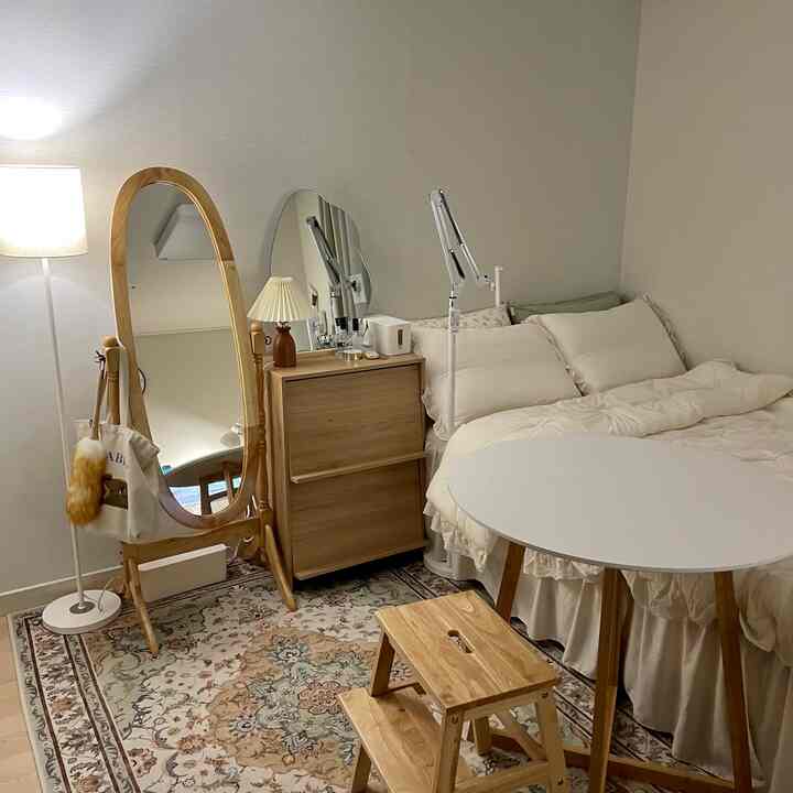 Natural-toned bedroom featuring wooden furniture, white bed, round table, and step stool creating a cozy atmosphere