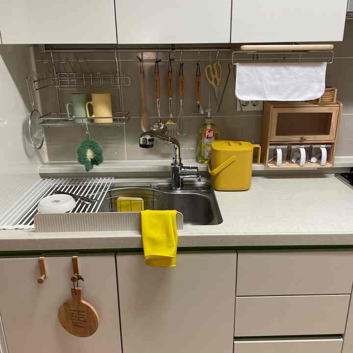 Clean kitchen with white and yellow tones, featuring a sink, hanging kitchen utensils, and organized storage solutions