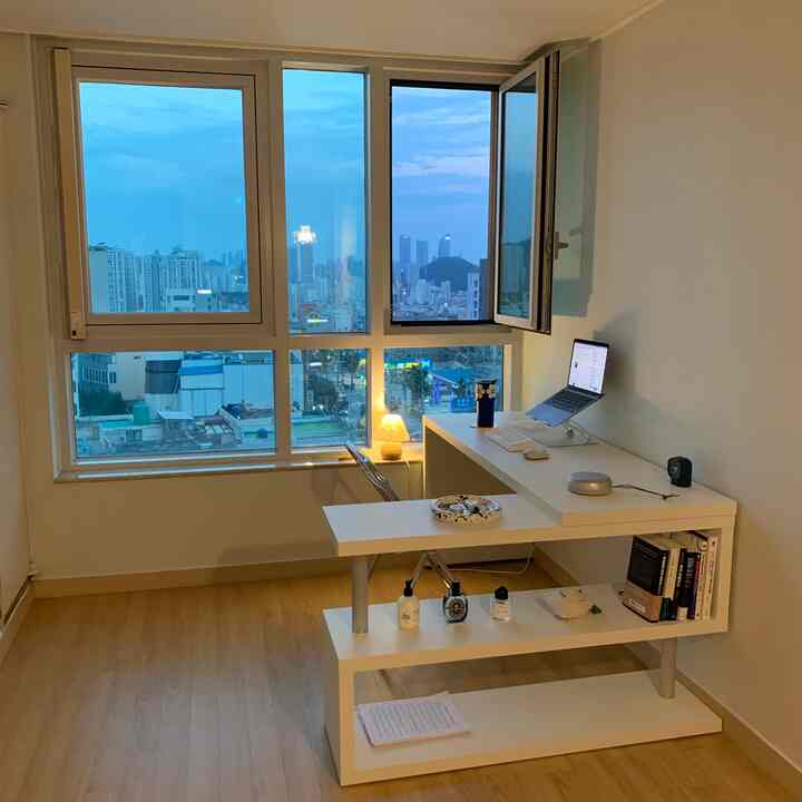 White and wood tone single household home office featuring a minimalist desk and chair by large windows with a cozy atmosphere