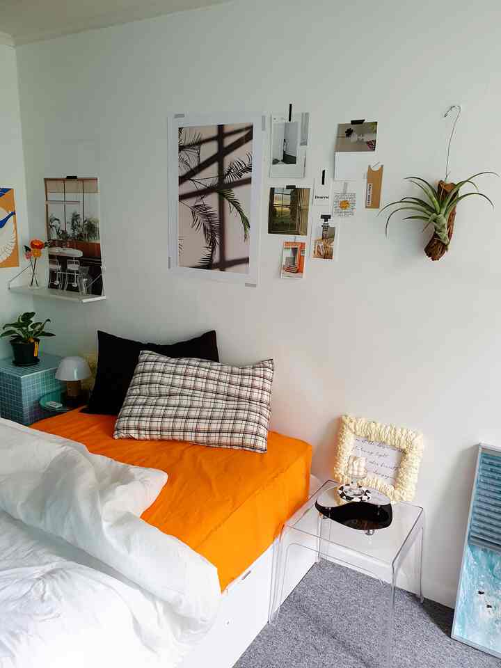 White and orange toned studio bedroom featuring bed, wall posters, and plants in a cozy setting