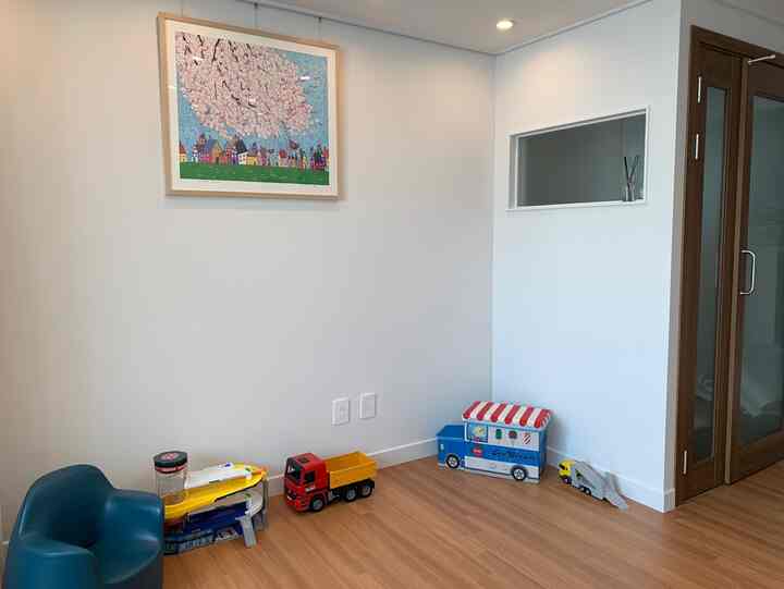 Living room corner with white walls and wood tone flooring, featuring kids' toys and artwork as focal points in a clean space