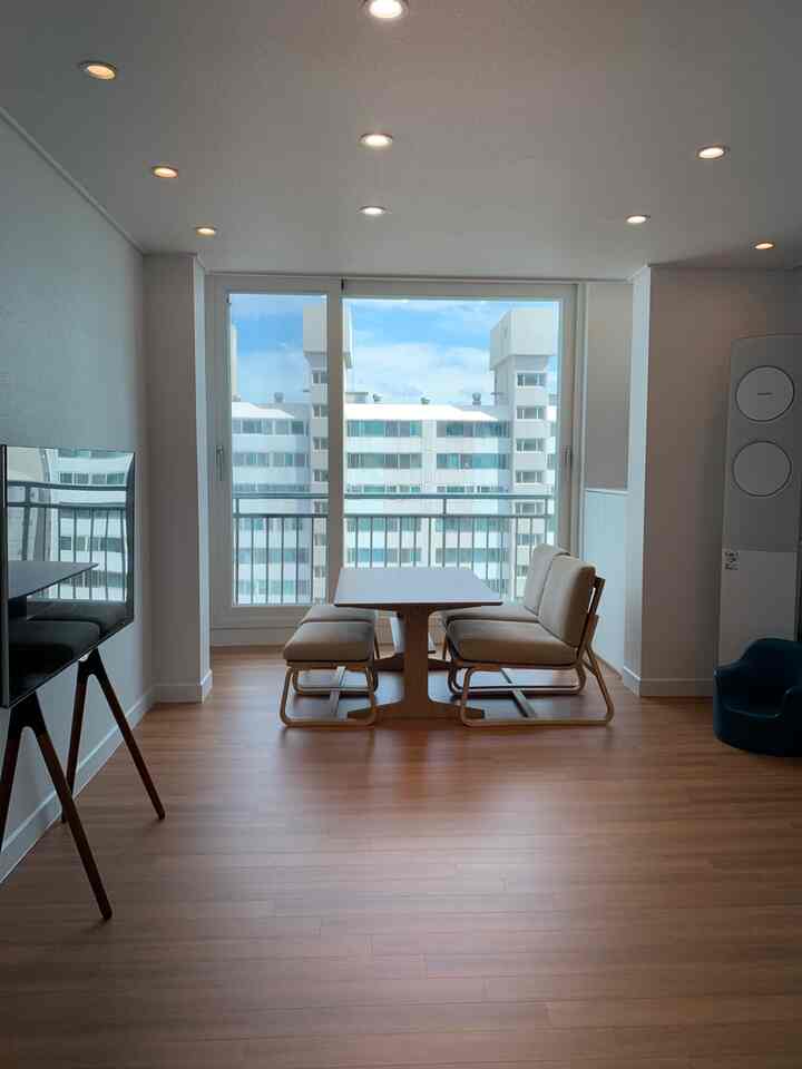 Natural tone living room with extended veranda window, wooden dining set, and easel-style TV stand in a simple modern space