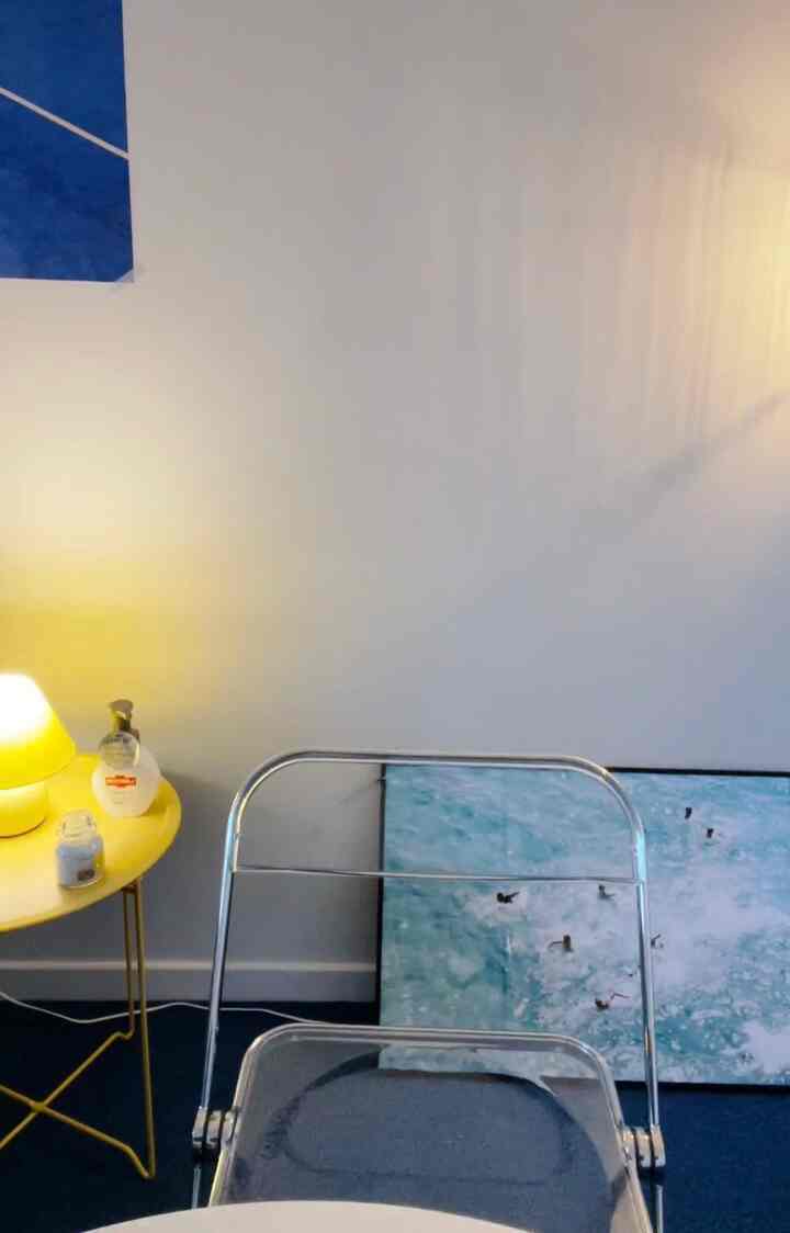 白い壁と青いカーペットのミニマルなホームオフィス空間、透明な椅子と黄色のサイドテーブルが配置された印象的なインテリア