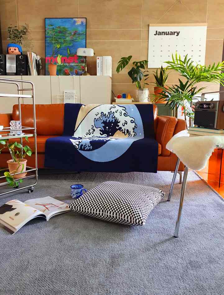 A cozy living room featuring a camel sofa and a gray rug, accented with plants and a calendar for a warm atmosphere