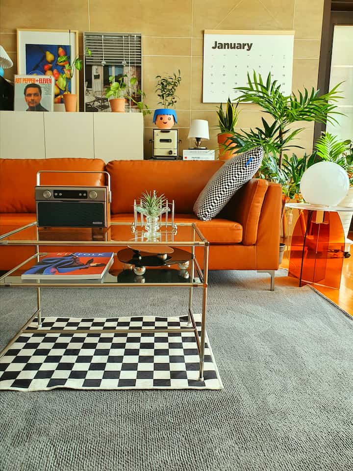 オレンジ色のレザーソファとグレーのラグが配置されたブラウン系のリビング、植物とポスターが調和するモダンでナチュラルな空間