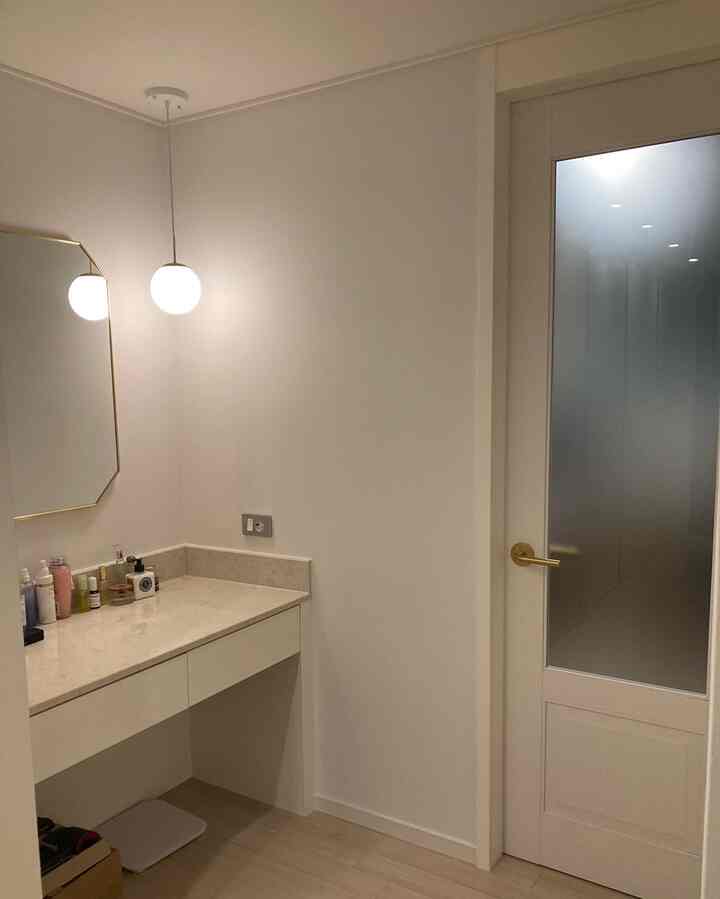 White-walled master bedroom dressing area featuring vanity with gold-accented mirror and pendant light, clean and modern ambiance