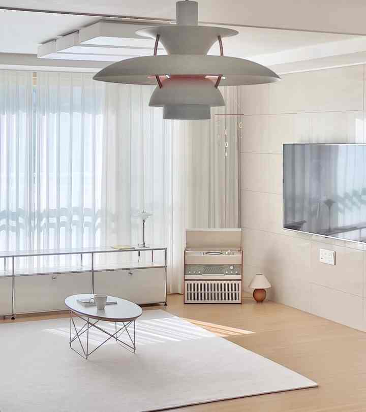 Modern living room with white and wood tones featuring pendant light, wall-mounted TV, transparent console, and a large rug creating a clean atmosphere