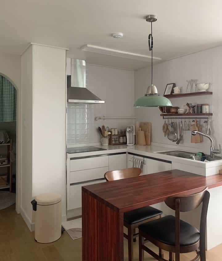 白い壁と濃い木製のダイニングチェアが配置されたナチュラルモダンなL字型キッチンのインテリア