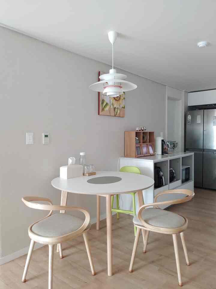 Modern dining room with white and natural wood tones featuring a round table, armchairs, and a pendant light