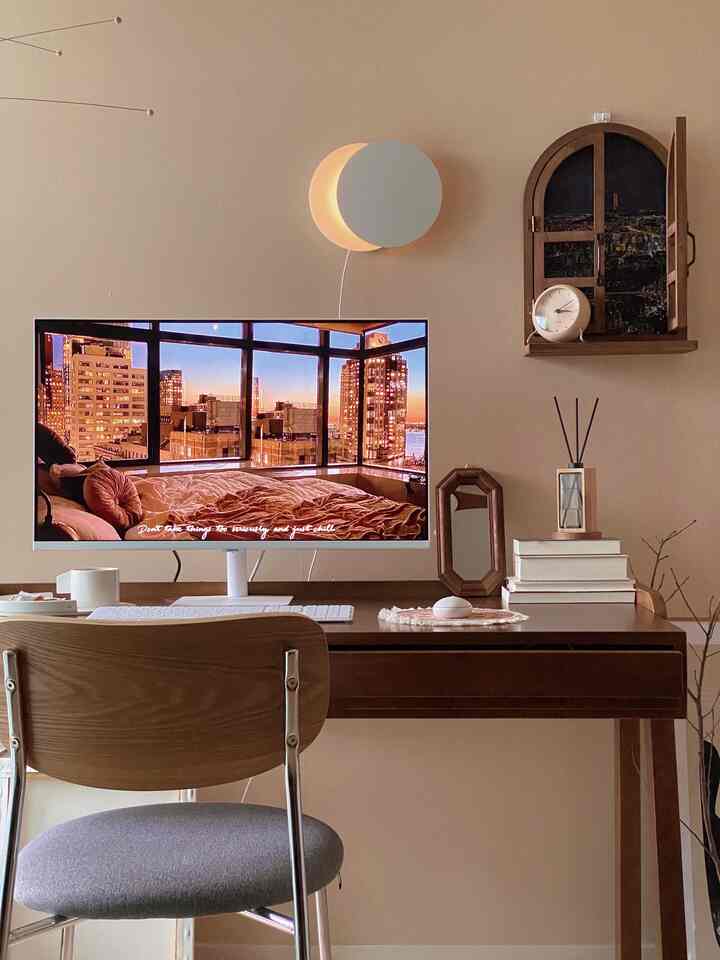 ベージュの壁と木製家具のある書斎、月の形の壁灯と机上のディフューザー、卓上時計が配置された雰囲気のあるインテリア