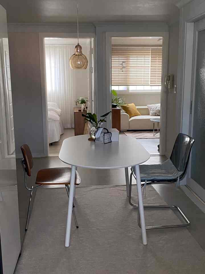 Modern two-person dining space in white and wood tones, connecting a living room and bedroom with minimalistic design