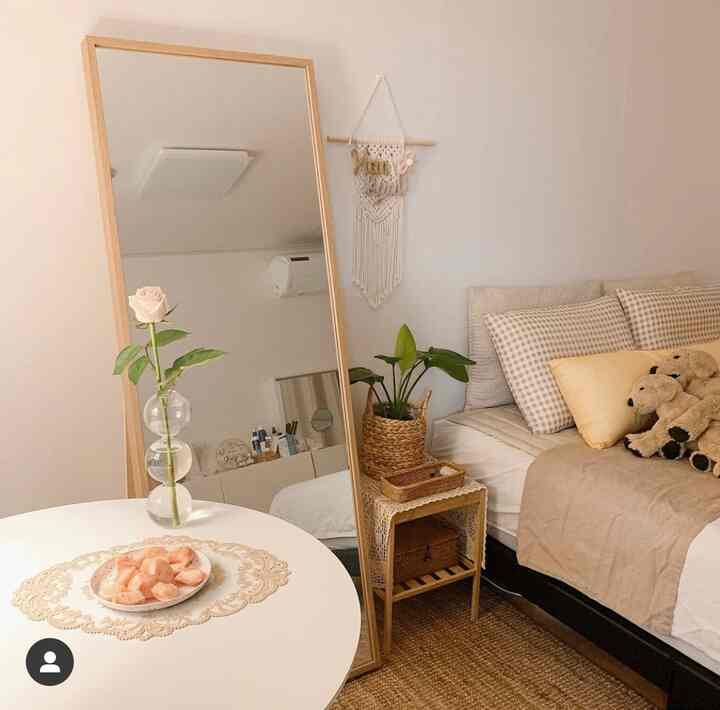 白と木目調の寝室、円形テーブルと全身鏡、ラタンラグと自然を感じる植物が配置された雰囲気のある空間