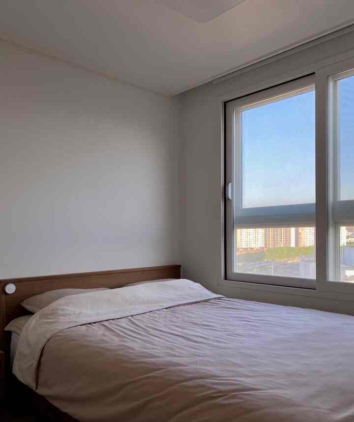 A simple and clean bedroom in white and brown tones with natural light coming through the window