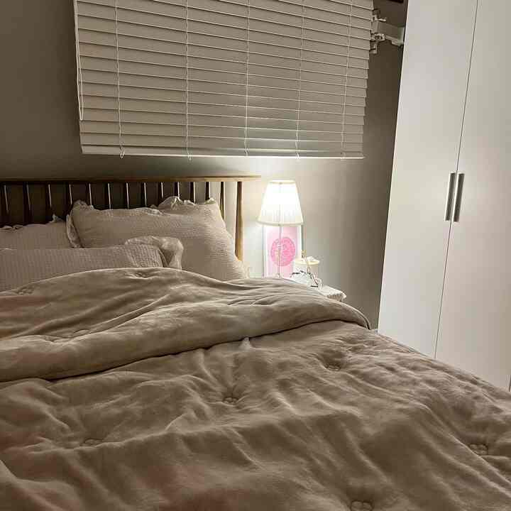 Natural wood tone and white bedroom featuring a wooden bed frame, beige microfiber bedding, and white wardrobe creating a calm atmosphere