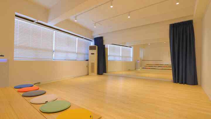 Bright wood-tone flooring and white blinds in a minimal practice space with blue blackout curtains accenting a spacious room