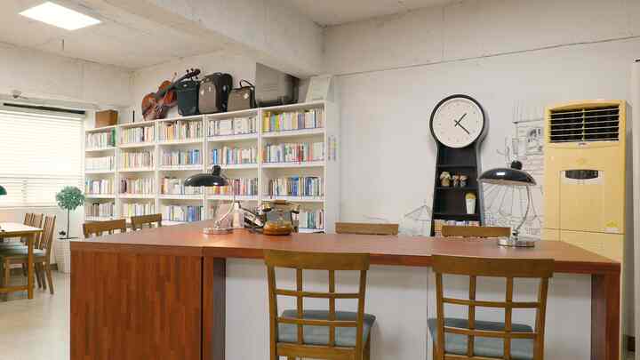 White and brown toned study and living space featuring a central wooden desk with chairs and large bookshelves in the background, cozy atmosphere