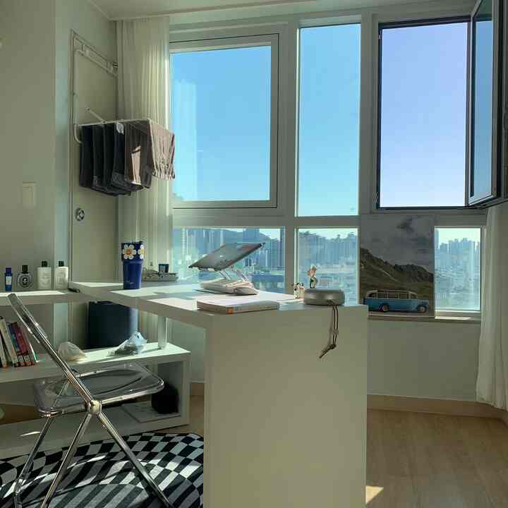 Bright small home office with white and wood tones, featuring large windows and tidy desk arrangement creating a cozy atmosphere