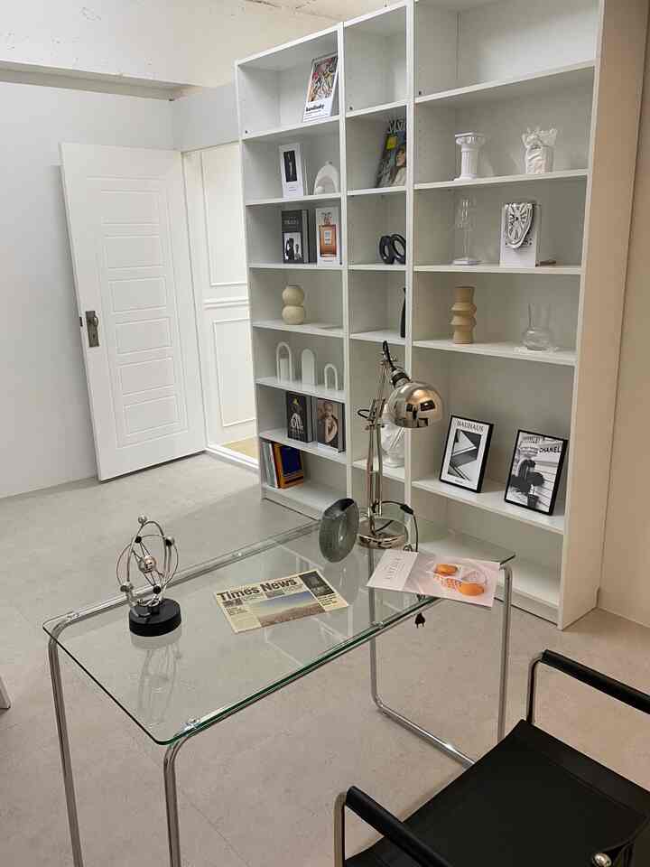 A simple, modern home office with transparent glass desk and large white bookshelf in white&black tones.