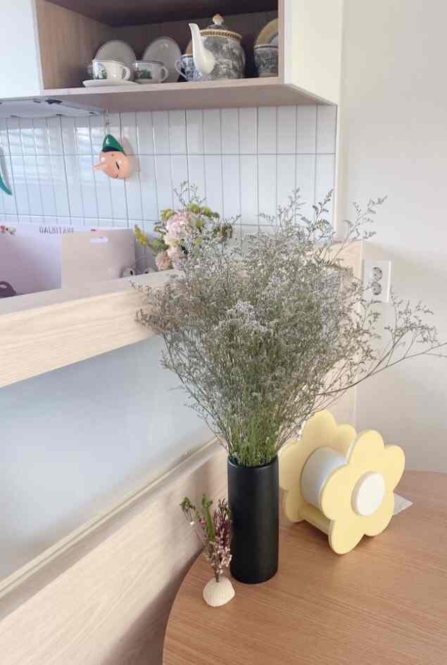Natural kitchen space featuring a wood-tone dining table with a black vase and yellow flower-shaped tissue holder