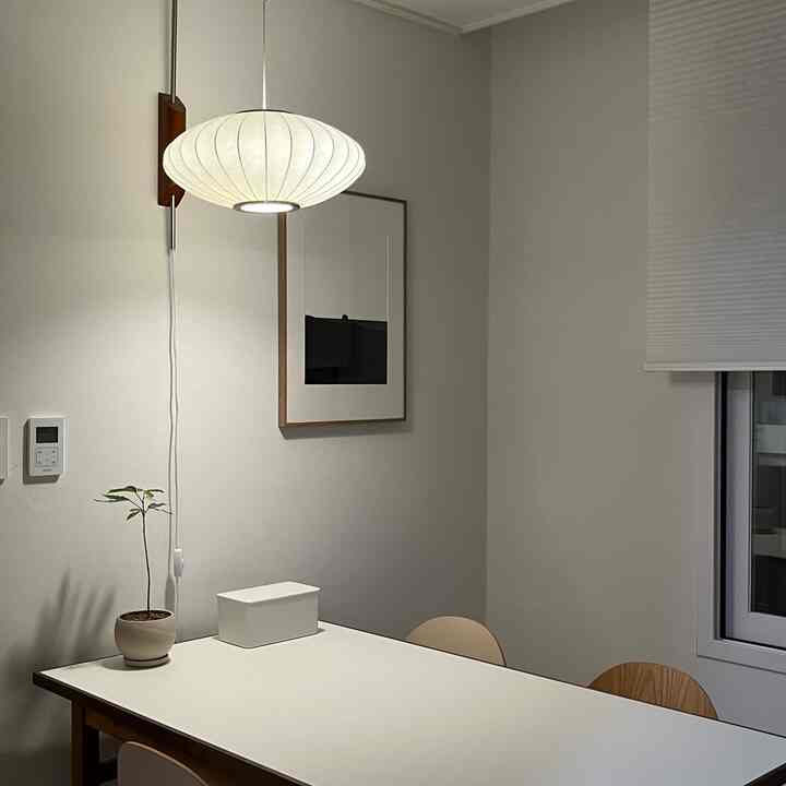 白とナチュラルカラーのダイニングルーム、壁照明と額縁が配置されたシンプルなインテリア