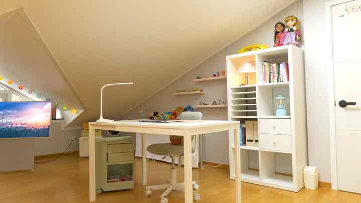 Cozy small home office with white and natural wood tones under a prominent slanted ceiling, featuring a desk and organized storage units