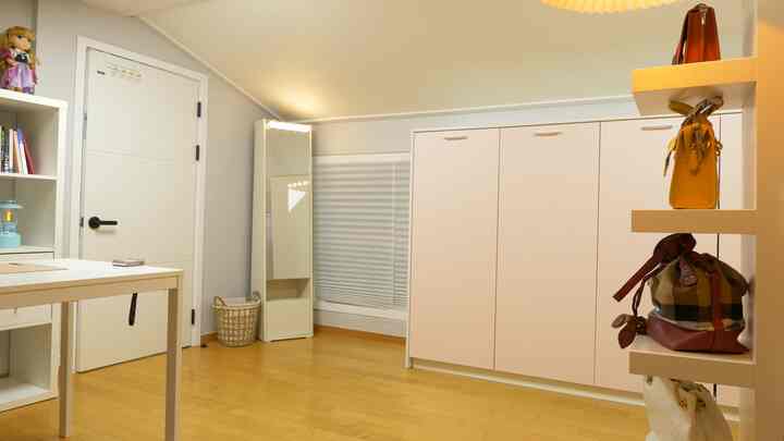 Small studio apartment with white and wood tones, featuring a large closet, full-length mirror, and a simple desk setup