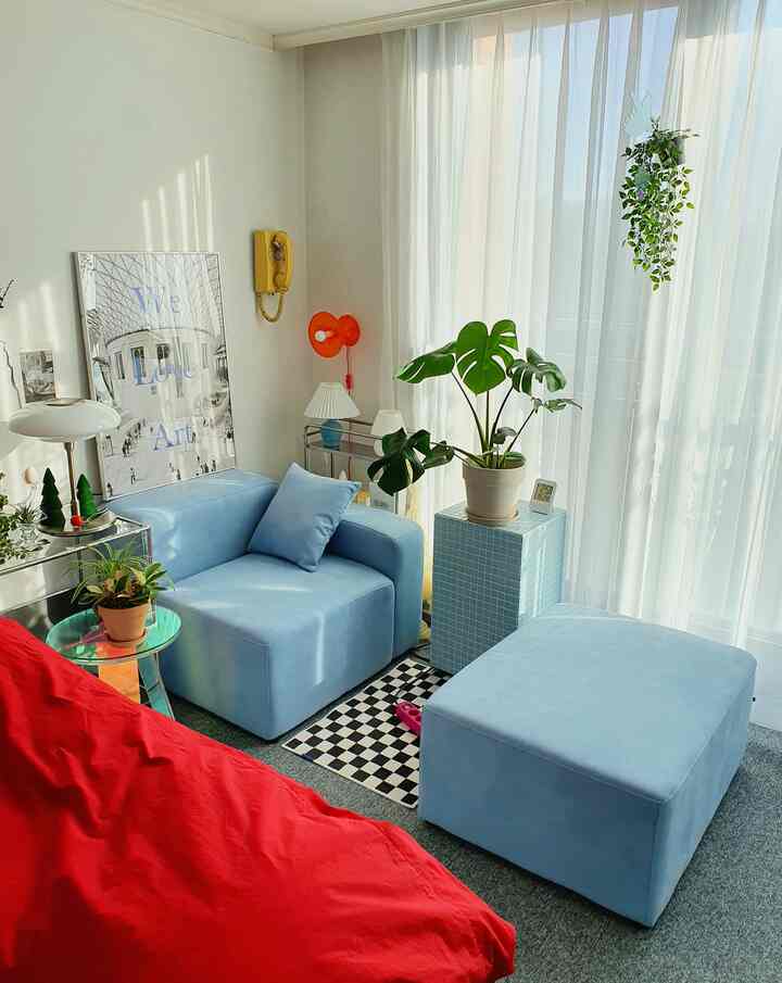 A white and blue-toned living room connected to a veranda featuring an aquatex single sofa and stool, various plants arranged in a natural modern space