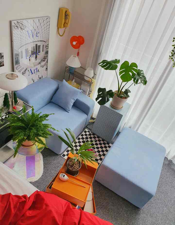 A white and blue toned living room featuring modular sofa, side tables, and several plants creating a natural and harmonious atmosphere.