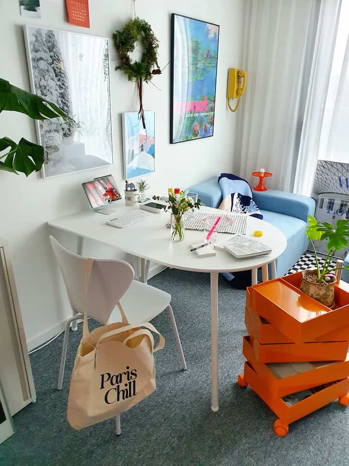 White and orange tones in a studio apartment space featuring a half-oval dining table and chairs arranged for neat work and reading setup