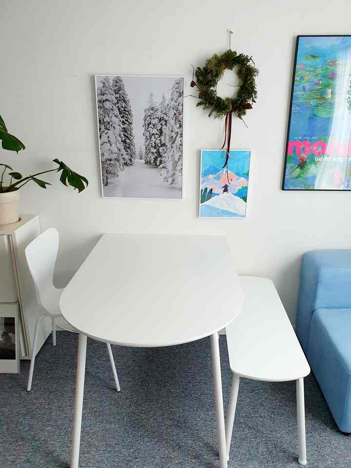 White-toned studio dining room featuring a white dining table and chairs, natural landscape artworks, and a simple, harmonious interior