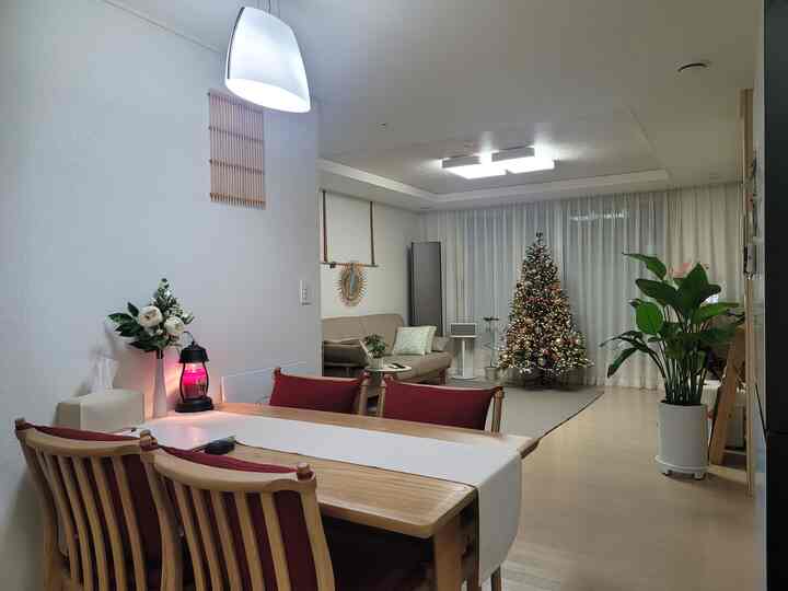 Bright white and wood-toned living and dining room featuring a Christmas tree, plants, and a warm cozy atmosphere