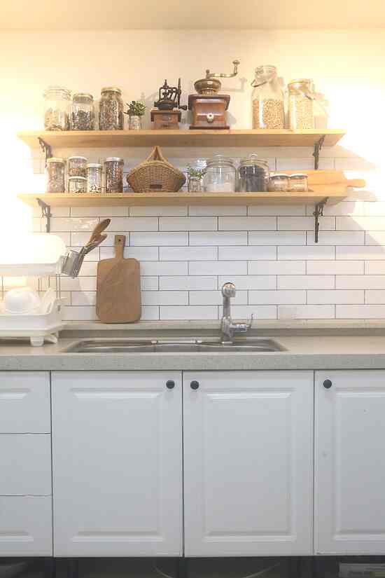 White and wood tone kitchen featuring shelves with glass bottles and a coffee grinder, creating a neat and cozy atmosphere