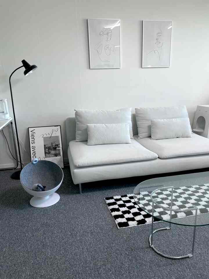 Gray and white toned studio living room featuring a white sofa and transparent glass coffee table in a clean, minimal setting