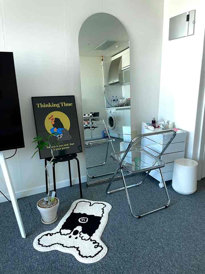 White and gray toned powder room featuring a full-length mirror, transparent stool, yellow poster, plant, and a cute rug in a simple setting