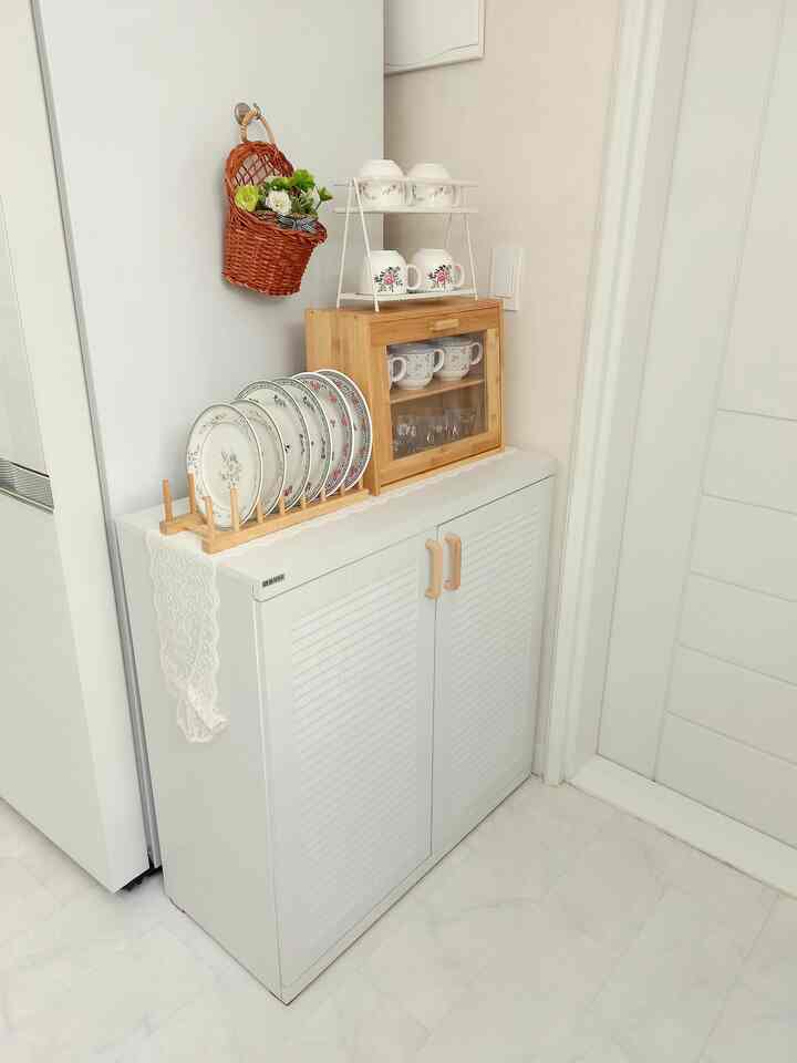 White and wood tone kitchen storage space featuring neatly arranged plates and mugs with a clean interior