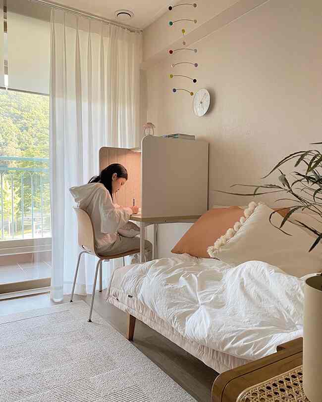 Bright wood tone and white kids' room with daybed on the right and child studying at desk on the left, creating a cozy atmosphere