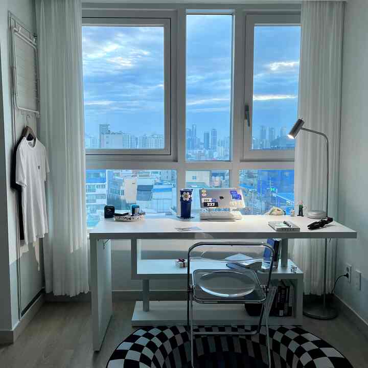 Clean studio home office with white and transparent furniture highlighted by large blue-toned windows
