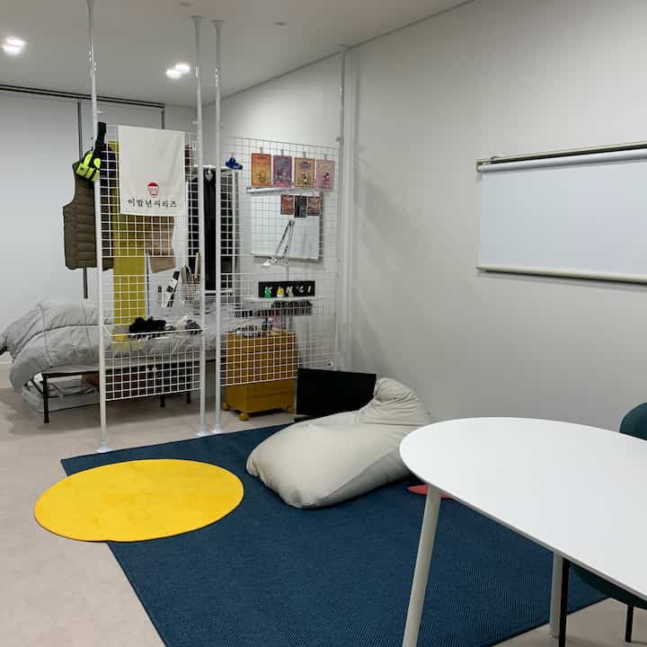 白とネイビートーンのワンルーム、ビーズクッションと多目的パーティションが配置された実用的な空間