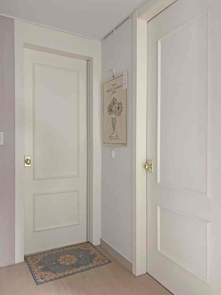 Entrance space featuring white tones and wood flooring, decorated with a poster and small floor mat creating a calm atmosphere