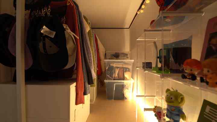 A narrow room with white tones featuring a clothing rack on the left and stacked transparent storage bins in the center, creating a practical storage area