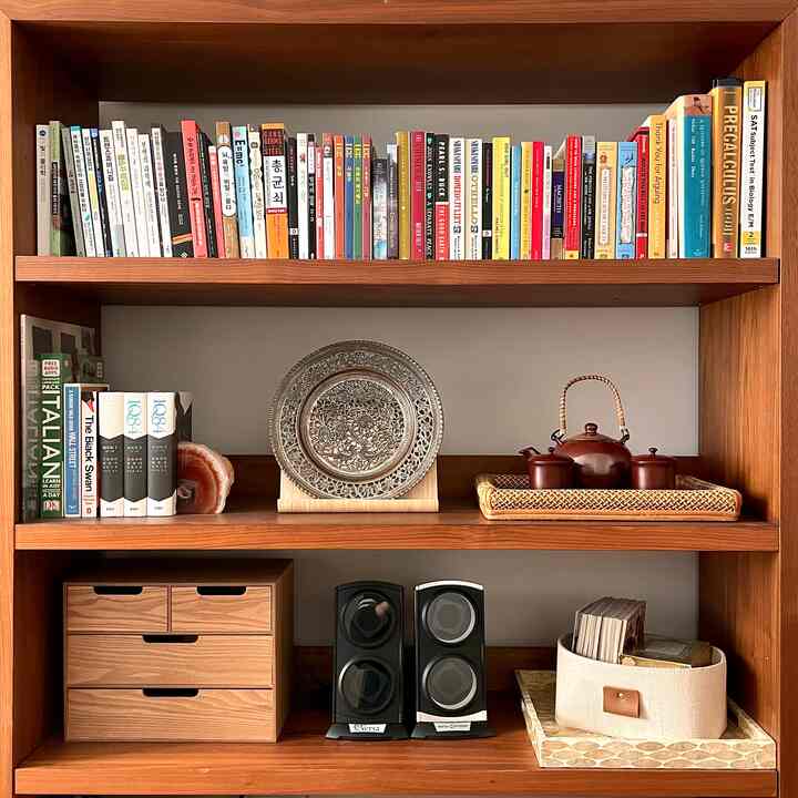 Brown wood-tone study bookshelf featuring diverse books, tea set, and wooden organizer arranged in a cozy space