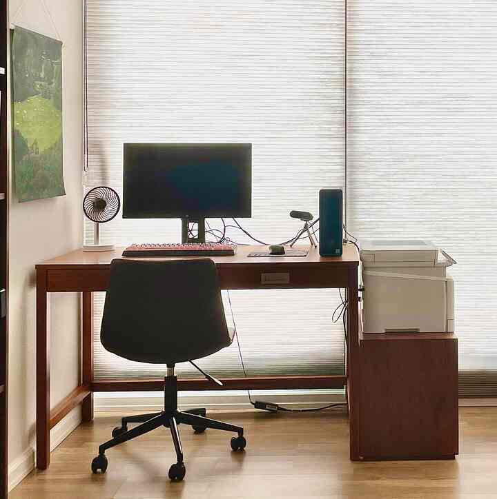 Brown wood tone study space featuring a simple desk and chair with a green fabric poster on the left, creating a neat home office atmosphere