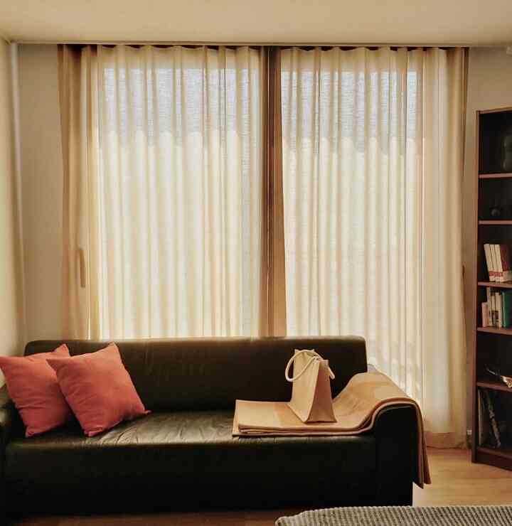 Beige and wood tone bedroom corner featuring linen curtains and a dark sofa creating a cozy natural atmosphere