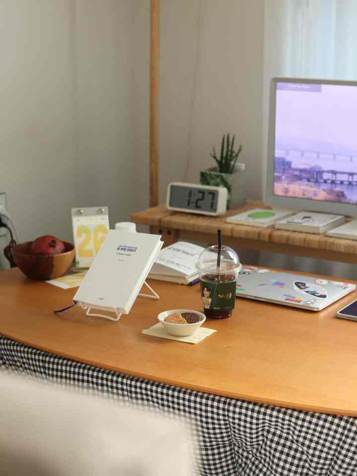 Natural wood-tone single household home office featuring a monitor, books, and a drink on a tidy workspace