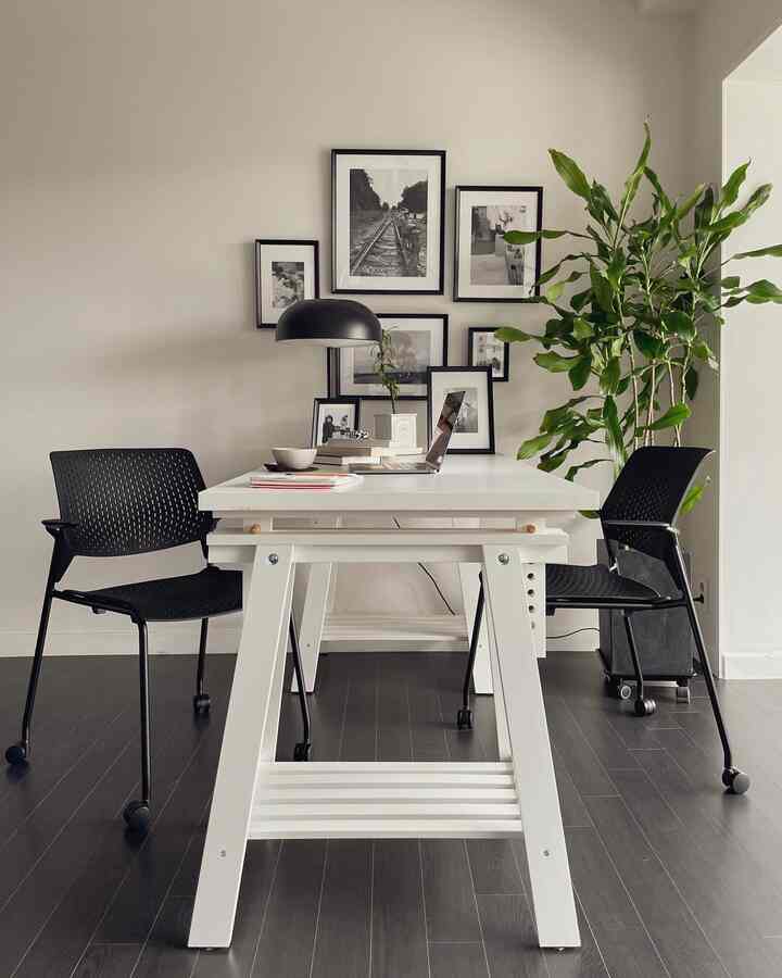 Modern and clean home office featuring a white desk and black office chairs centrally placed with picture frames decorating the wall behind
