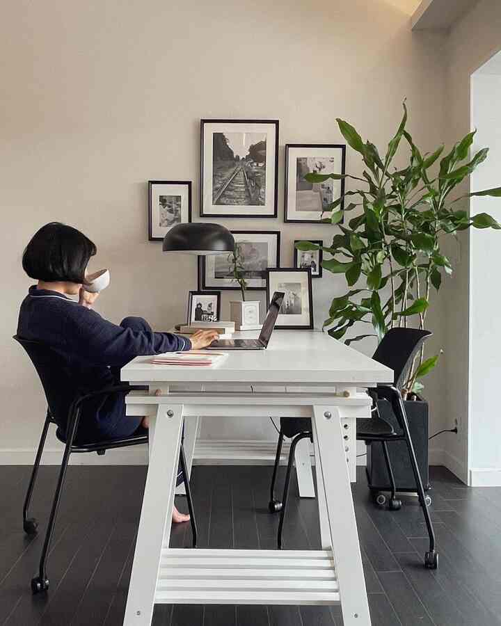 White and black toned workspace featuring mid-century modern desk and chairs with picture frames on the wall in a neat home office