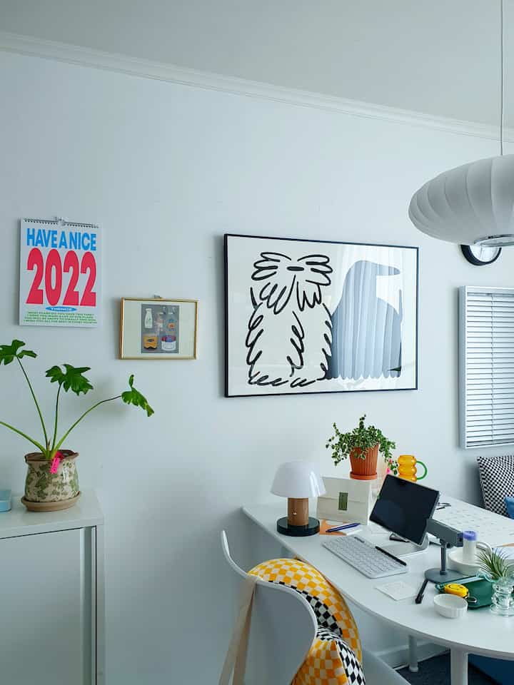 Minimal style home office with white walls featuring framed art and posters, clean desk adorned with plants