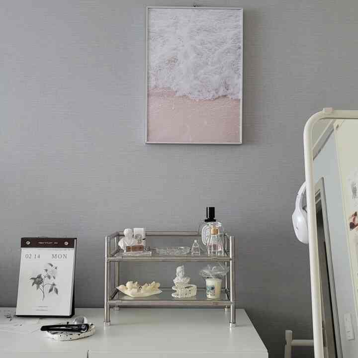 Gray wall background with white desk featuring a small metal storage shelf, pink beach poster on wall, and full-length mirror creating a clean interior
