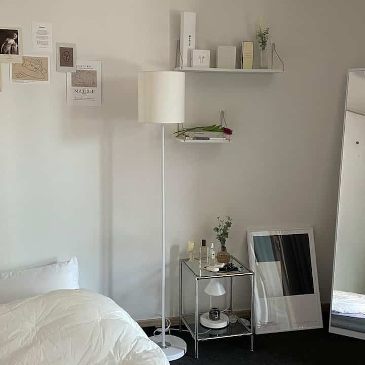 White and natural toned studio apartment bedroom featuring a simple modern floor lamp and metal nightstand in a cozy atmosphere
